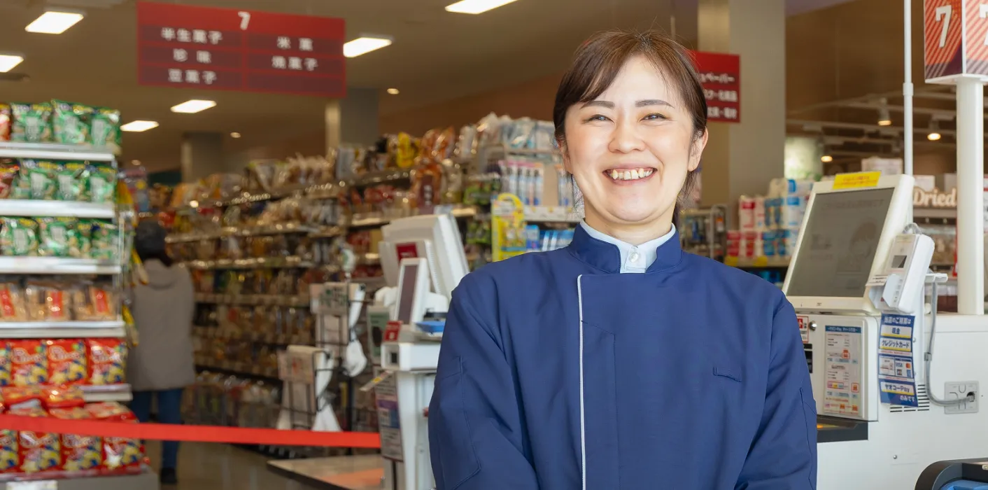 レジを背景に立ち、笑顔で正面を向いているY.Y.さん