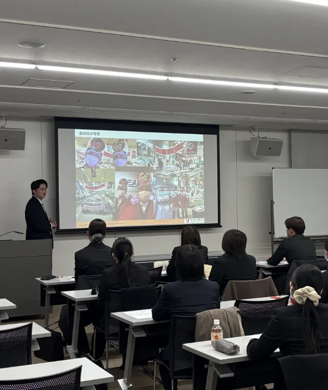 会議室で、プロジェクターに資料を映しながら講義をしている様子。10名弱の就活生が映っている。