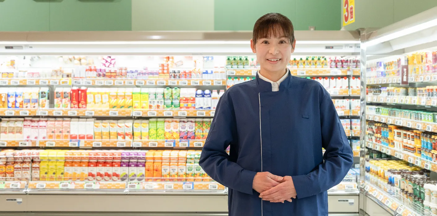 A.A.さんが日配商品を背にして笑顔で立っている様子