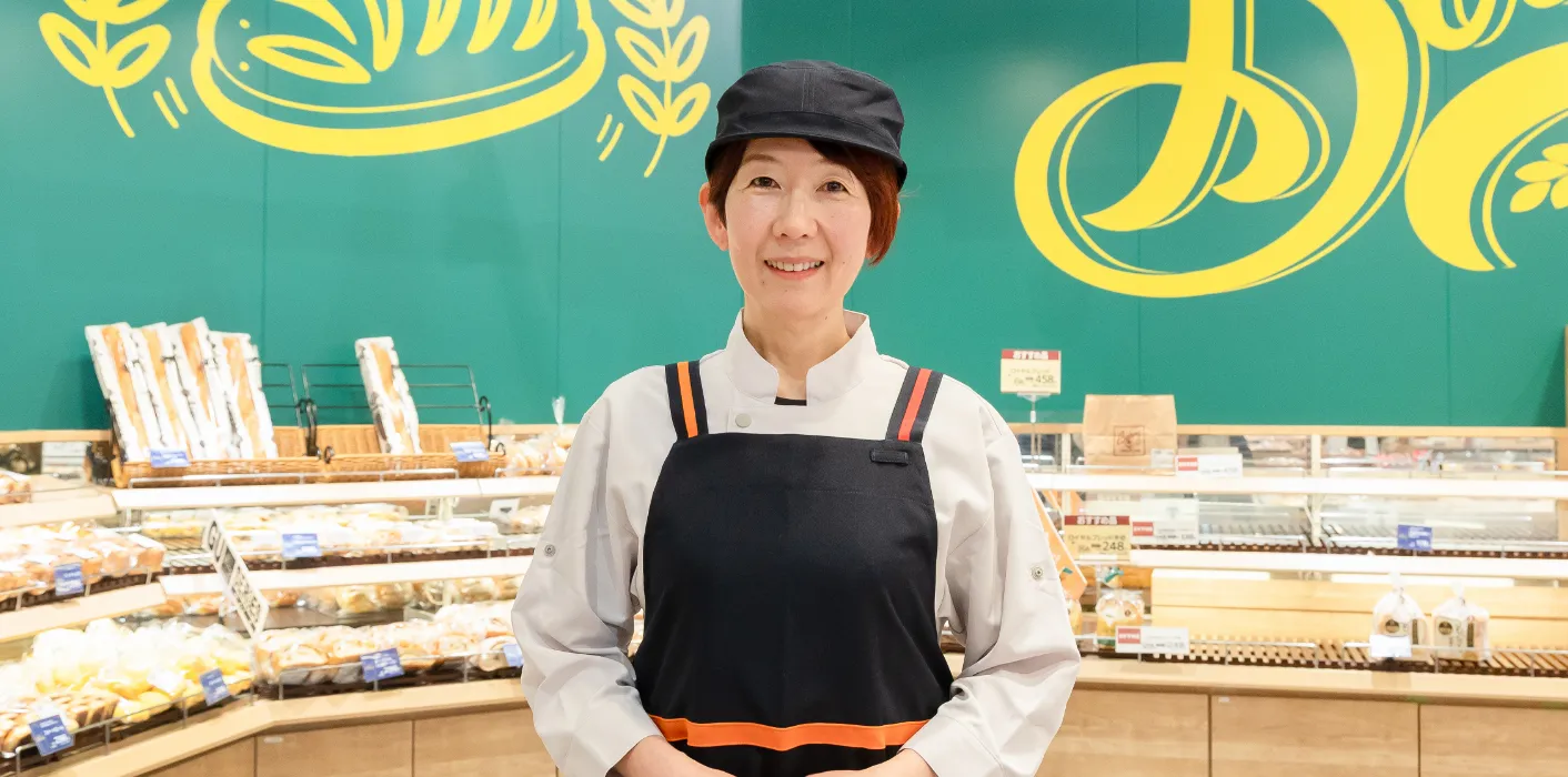 H.E.さんがベーカリーコーナーを背にして笑顔で立っている様子