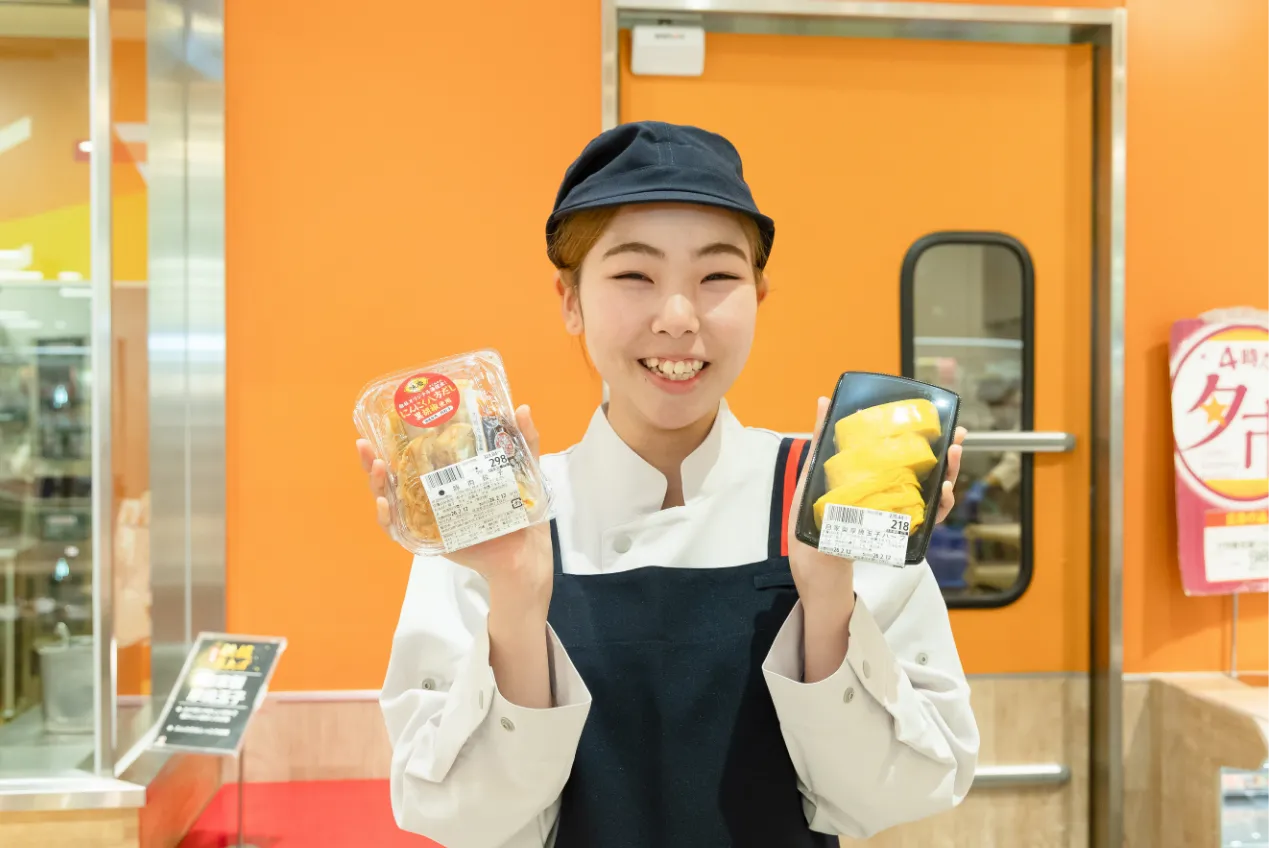 商品を両手に持って顔の横に掲げ、笑顔で立っている従業員の様子