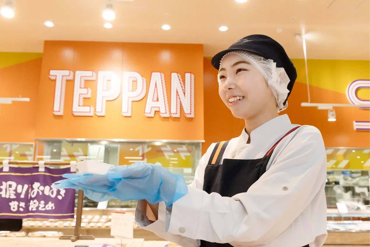 手袋をはめて試食用の小さなカップを持ち、お客様へお勧めしている従業員の様子