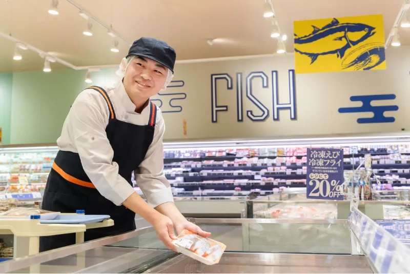 S.E.さんが鮮魚コーナーで品出しをしている途中で、お客様へ笑顔を向けている様子